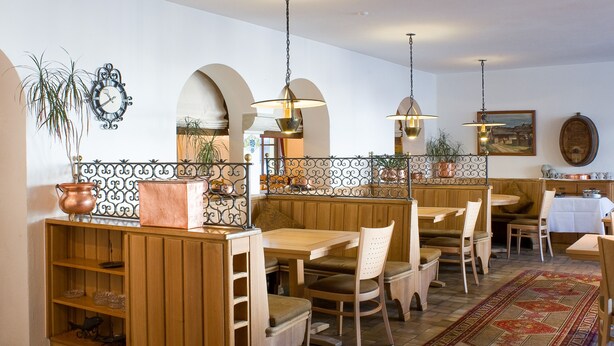 A restaurant with wooden furniture, a patterned rug, and decorative plants. - Hotel Post Bivio (Surses)