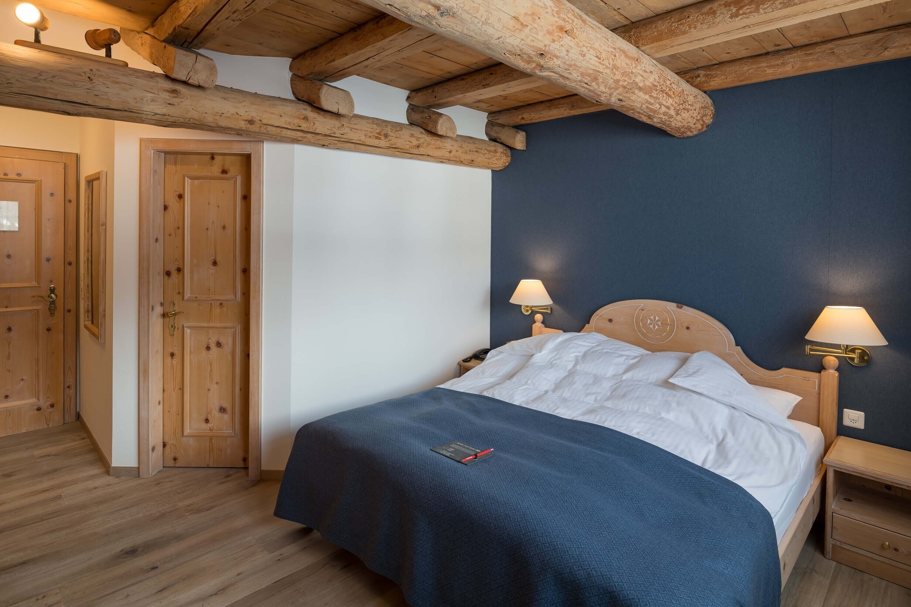 A bedroom with a wooden ceiling, a bed with white linens, two bedside lamps, and a nightstand.