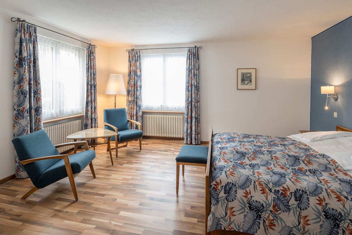 A hotel room with a bed, two armchairs, a small table, and a lamp.