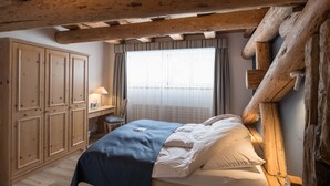 A bedroom with a wooden bed, a desk with a lamp, and a large window with curtains. - Hotel Post Bivio (Surses)