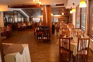 A restaurant with wooden tables and chairs, a wine rack, and large windows. - Club Hotel Yanakiev (Samokov)