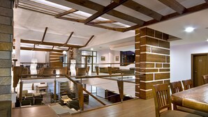 A spacious dining area with a high ceiling, wooden beams, and a brick accent wall. - Club Hotel Yanakiev (Samokov)