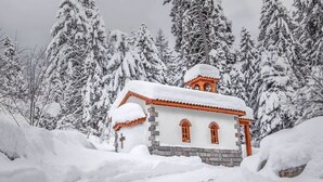 A snow-covered building with a clock tower, surrounded by snow-laden trees. - Club Hotel Yanakiev (Samokov)