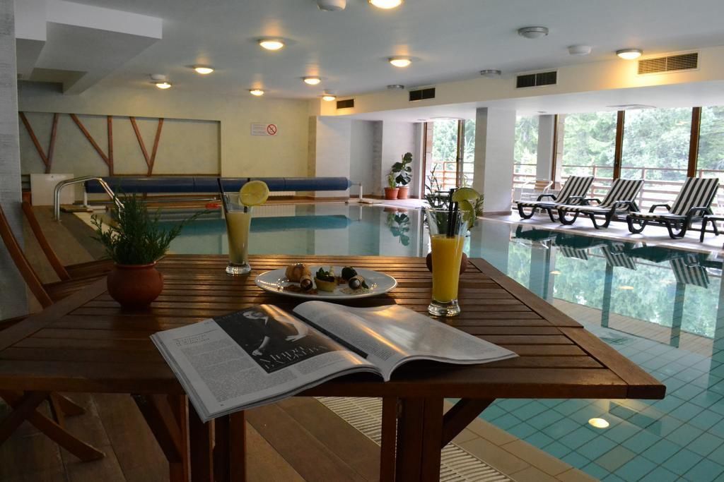 Un área junto a la piscina con una mesa de madera, una revista, un plato de comida y un vaso de jugo.