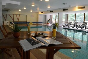 A poolside area with a wooden table, a magazine, a plate of food, and a glass of juice. - Club Hotel Yanakiev (Samokov)