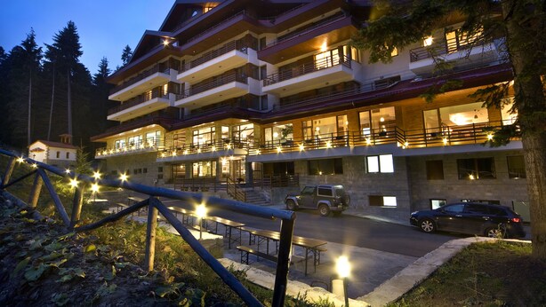 A multi-story hotel with balconies, outdoor seating, and a parking area. - Club Hotel Yanakiev (Samokov)