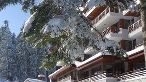 A multi-story building with balconies, surrounded by snow-covered trees. - Club Hotel Yanakiev (Samokov)