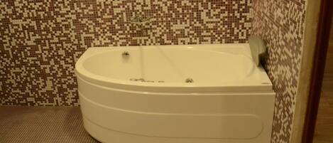 A corner bathtub with a mosaic tile wall.