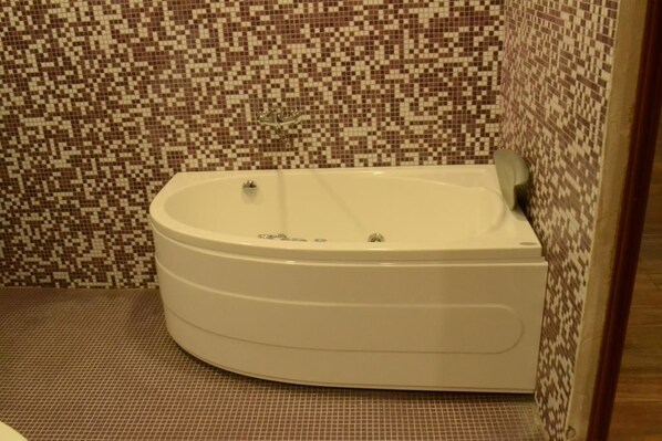 Une baignoire d’angle avec un mur recouvert de mosaïques.