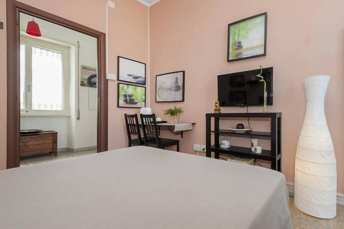 A bedroom with a bed, a desk, a chair, a TV, and a large mirror.