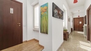 A hallway with wooden flooring, white walls, and a door with a sign. There are two paintings on the wall and a window with blinds. - Il Bacio delle Stelle (Rome)