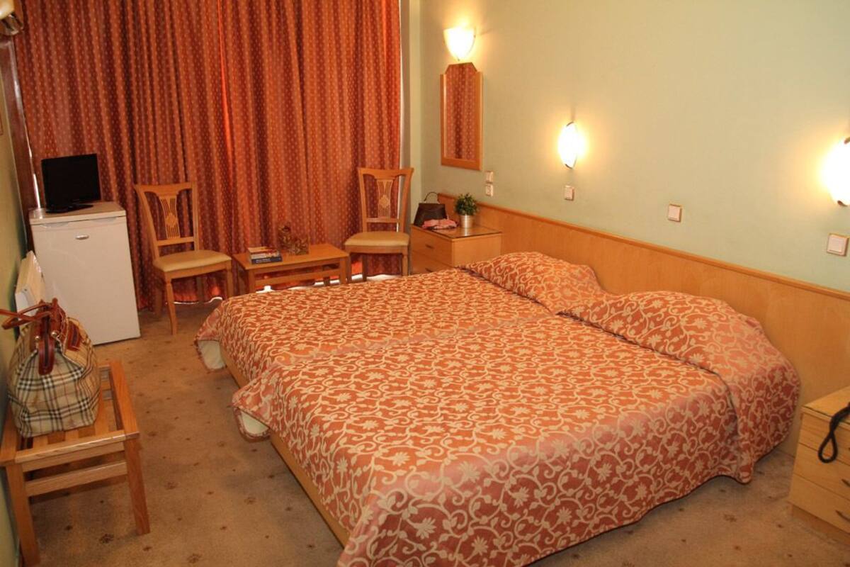A hotel room with a bed, a desk, a chair, a television, and a dresser.
