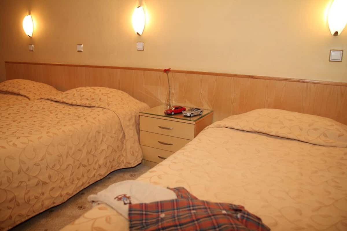 A hotel room with two beds, a nightstand, and wall-mounted lights.