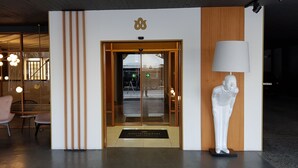 Entrada de hotel con puerta de madera, mostrador de recepción y estatua de un hombre.