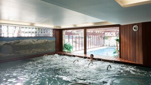 Un área de hidromasaje con vistas a una piscina exterior y un mural en la pared.