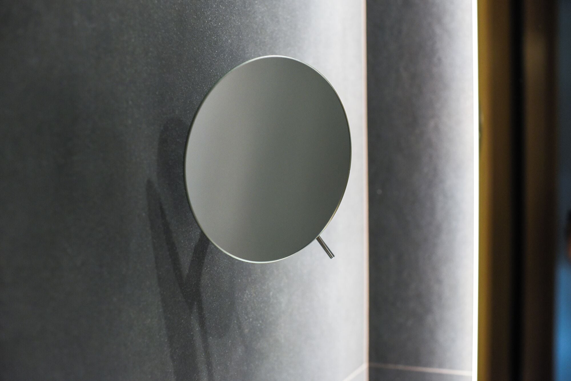 Un espejo circular con asa, sujeto a una pared texturizada.