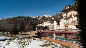 Un hotel con zona de piscina, terreno cubierto de nieve y montañas al fondo.