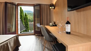 Habitación de hotel con escritorio de madera, una botella de vino y vista a zonas verdes.