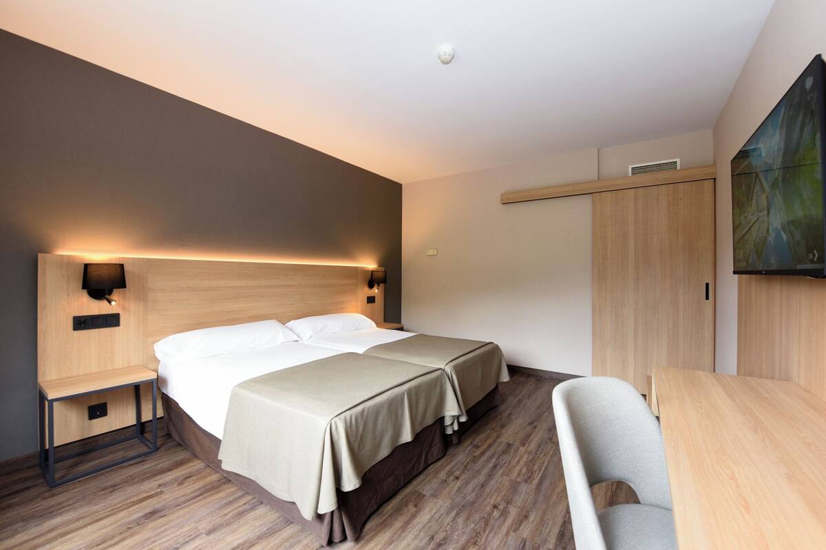 Una habitación de hotel con una cama grande, mesitas de noche, un escritorio y una silla.