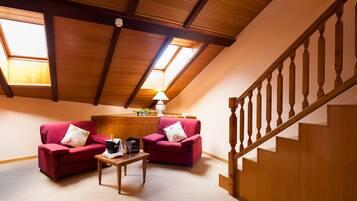 Una habitación acogedora con techo inclinado, vigas de madera, una escalera y dos sofás rojos.