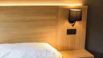 Un lit bien fait, avec du linge de lit blanc, une tête de lit en bois et une lampe fixée au mur.