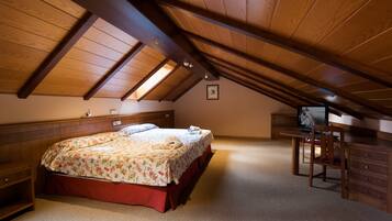 Een slaapkamer met een schuine plafond, een bed met bloemenbedrukking, een bureau met stoel en een televisie.