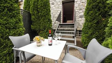 Una mesa al aire libre con una botella de vino, dos copas y un jarrón de flores.
