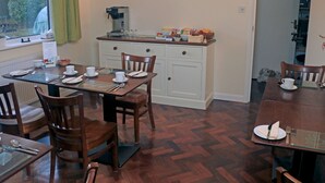 Un comedor con mesas y sillas de madera, una encimera de cocina con electrodomésticos y un cuadro en la pared.