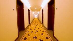 Un pasillo de hotel con alfombra estampada, puertas de madera e iluminación en el techo.