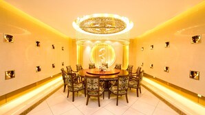 Un comedor lujoso con una mesa redonda, sillas ornamentadas, una araña y un gran número '3' iluminado en la pared.