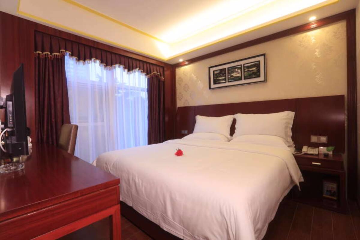 A hotel room with a large bed, a wooden desk, a nightstand, and a wall-mounted TV.