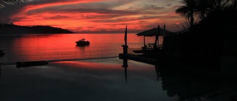 A sunset over a calm body of water with a boat and a dock with umbrellas.