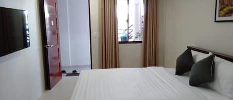 Un dormitorio con cama, televisión montada en la pared, una puerta y una ventana con cortinas.