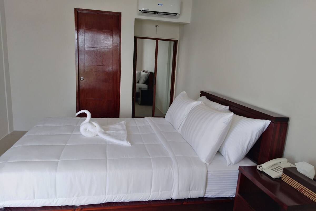 A neatly made bed with a swan-shaped towel, a bedside telephone, and a mirror in the room.