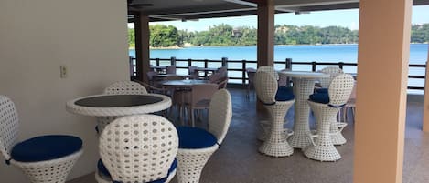 A covered outdoor seating area with wicker furniture and a view of the sea.