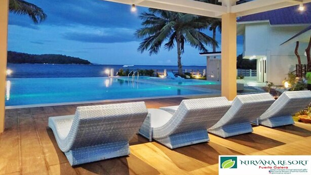 A poolside area with lounge chairs, a view of the ocean, and a building in the background. - Nirvana Resort (Puerto Galera)