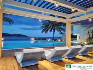 A poolside area with lounge chairs, a view of the ocean, and a building in the background. - Nirvana Resort (Puerto Galera)