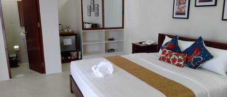 A hotel room with a large bed, a wooden wardrobe, a bedside table with a lamp, and framed pictures on the wall.