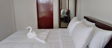 A hotel room with a bed, a wooden door, a wardrobe, and a mirror.