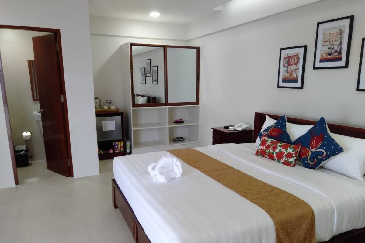 A hotel room with a bed, a bedside table, a nightstand, a wardrobe, and a mirror.