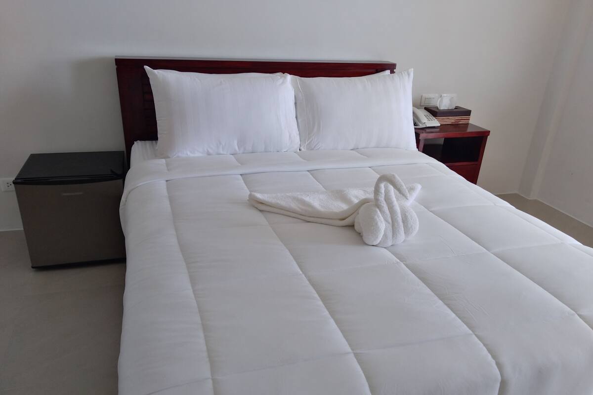 A neatly made bed with white bedding and a towel shaped like a swan.