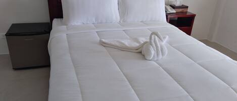 Un lit bien fait, avec du linge de lit blanc et une serviette en forme de cygne.