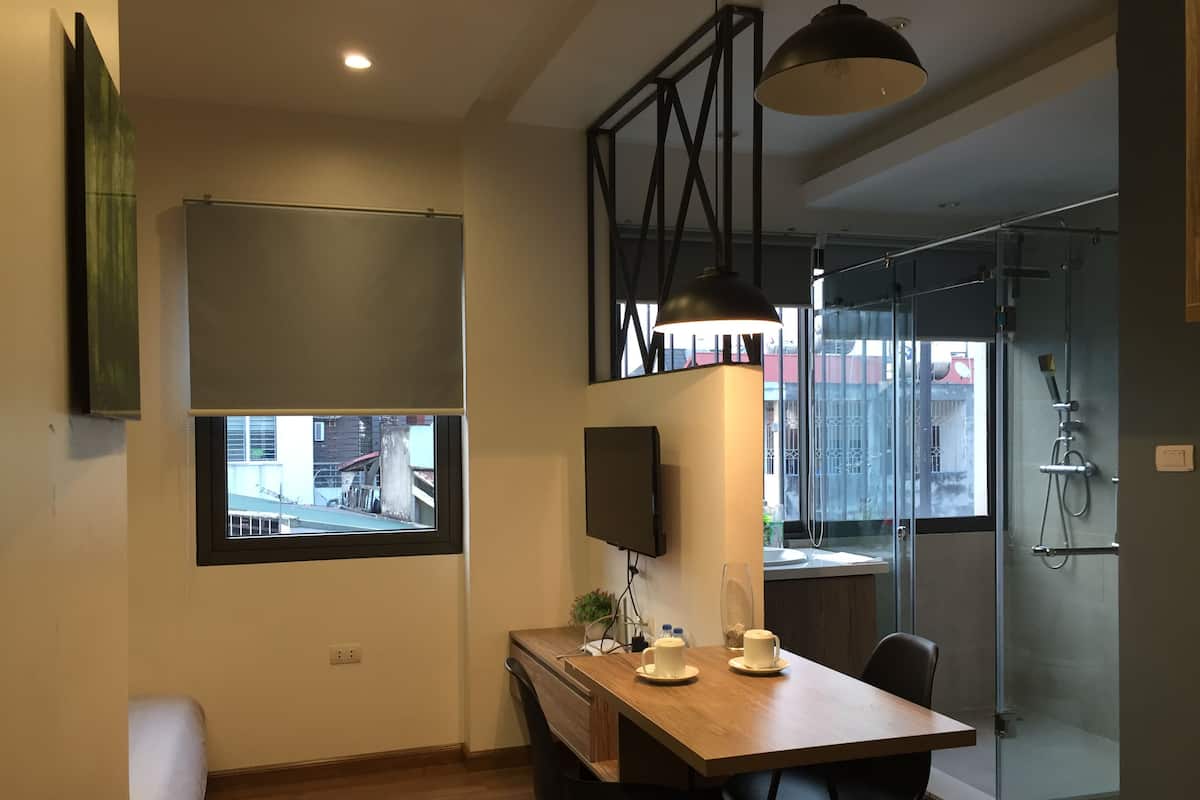 A modern kitchen with a wooden table, black chairs, a TV mounted on the wall, and a window overlooking a cityscape.