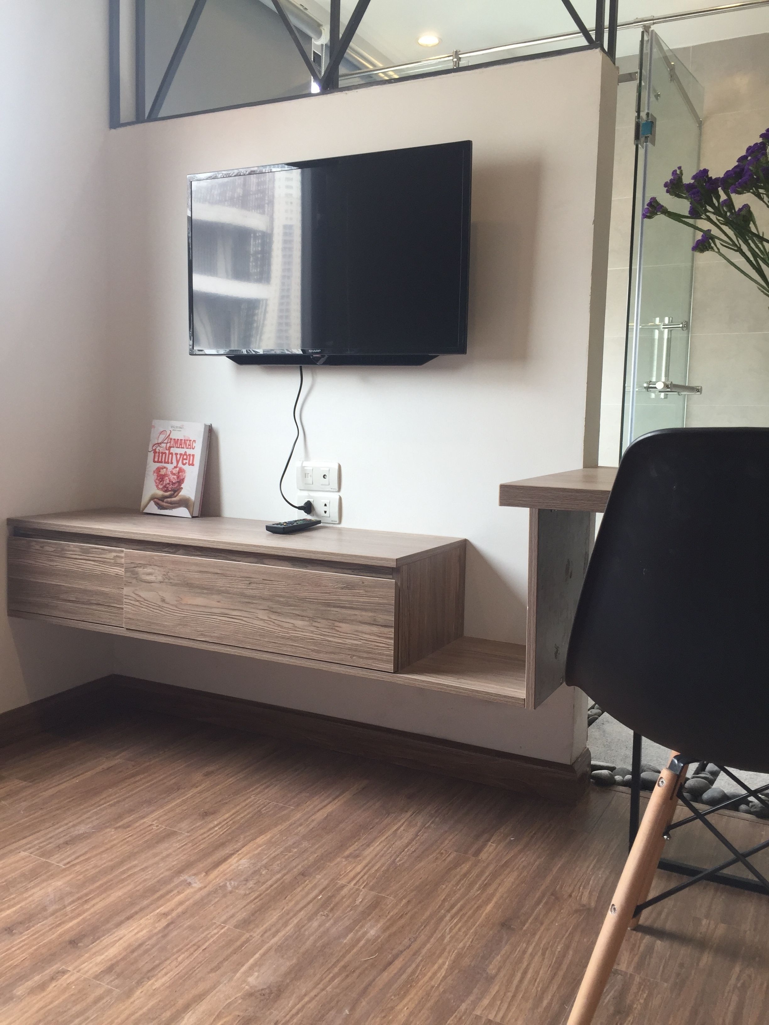A modern room with a built-in wooden desk, a mounted flat-screen TV, and a glass shower door.