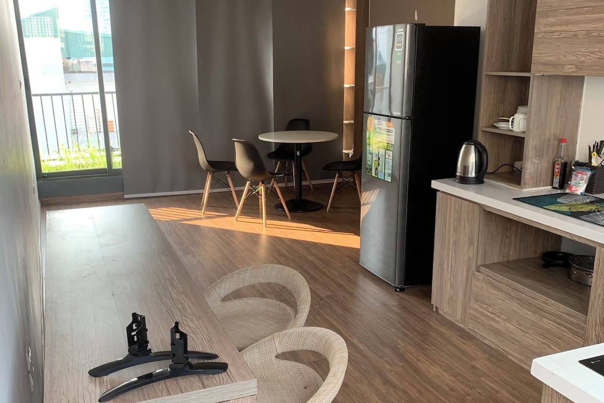 A modern kitchen with wooden cabinets, a dining area with a round table and chairs, and a refrigerator.