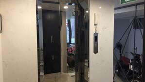 A modern elevator with a digital display, a glass door, and a sign indicating an exit. - Unique Serviced Apartment (Hanoi)