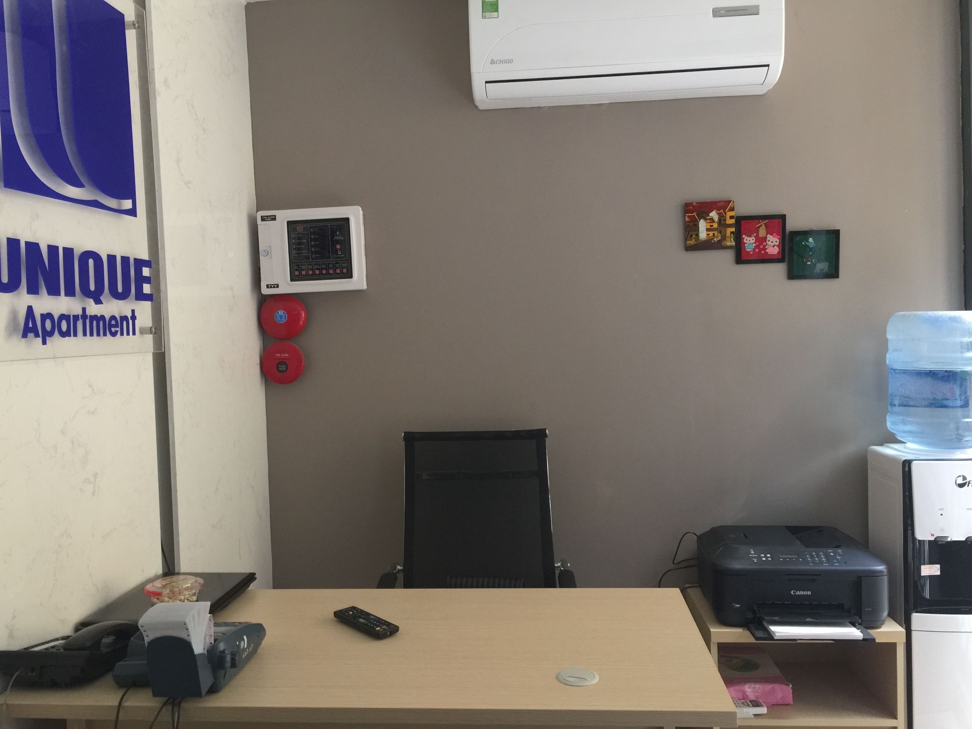 A hotel room with a desk, a printer, a water dispenser, and a wall-mounted air conditioner.