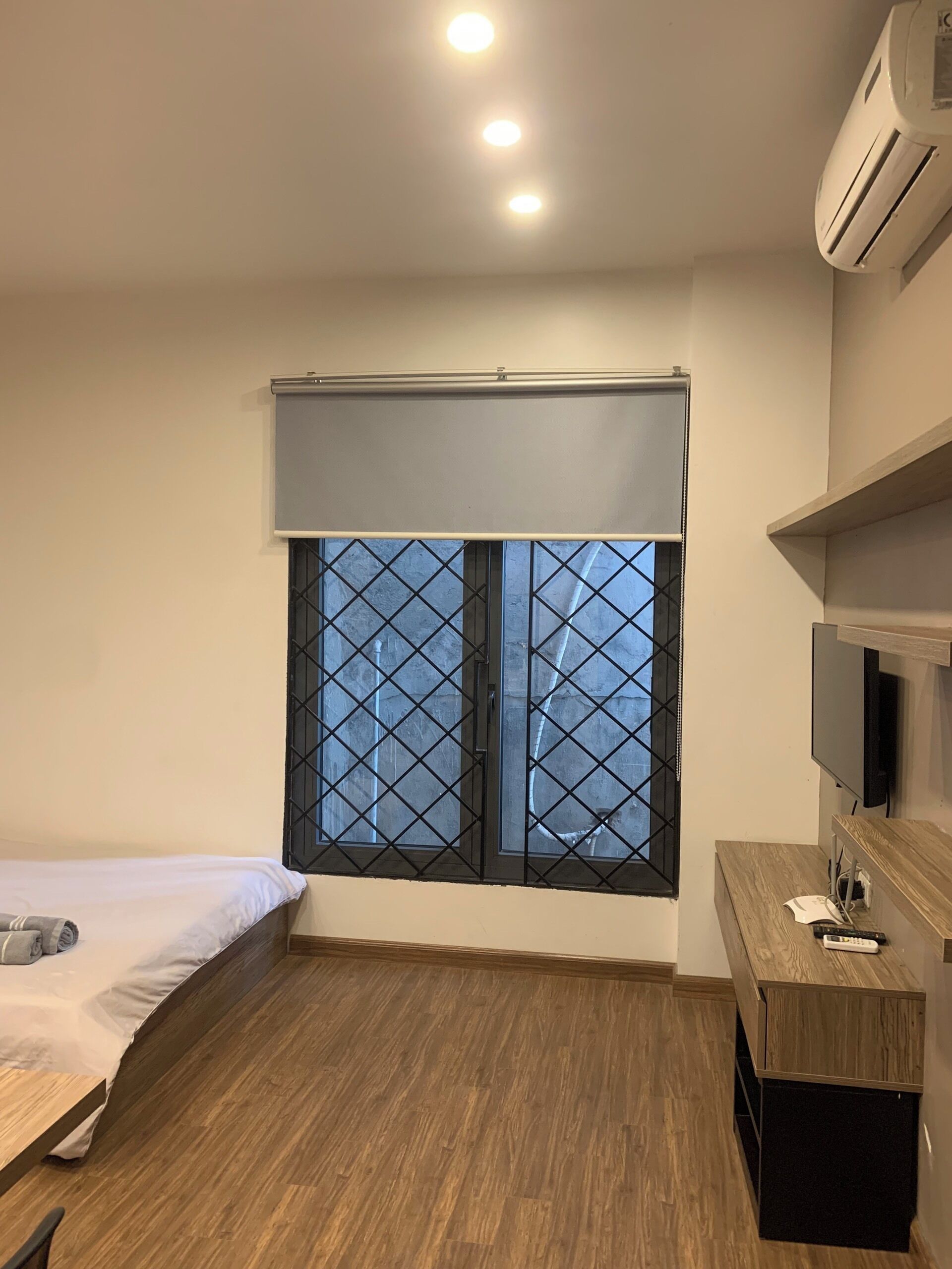 Une chambre d’hôtel avec un lit, un bureau en bois, une télévision et une fenêtre munie d’une grille métallique.