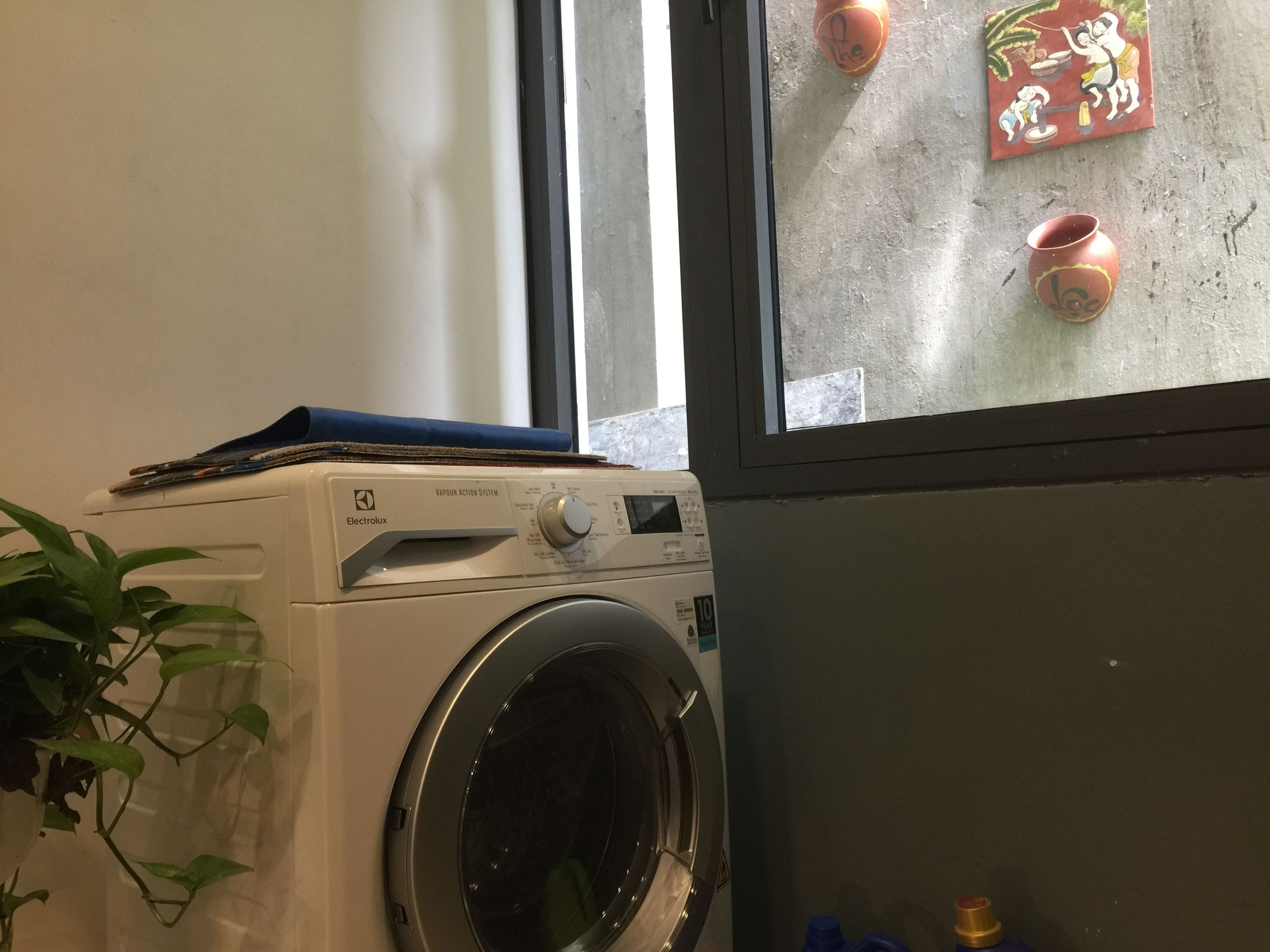 Una lavadora de carga frontal con un panel de control, una ventana con vistas al exterior y un adorno colgado en la pared.