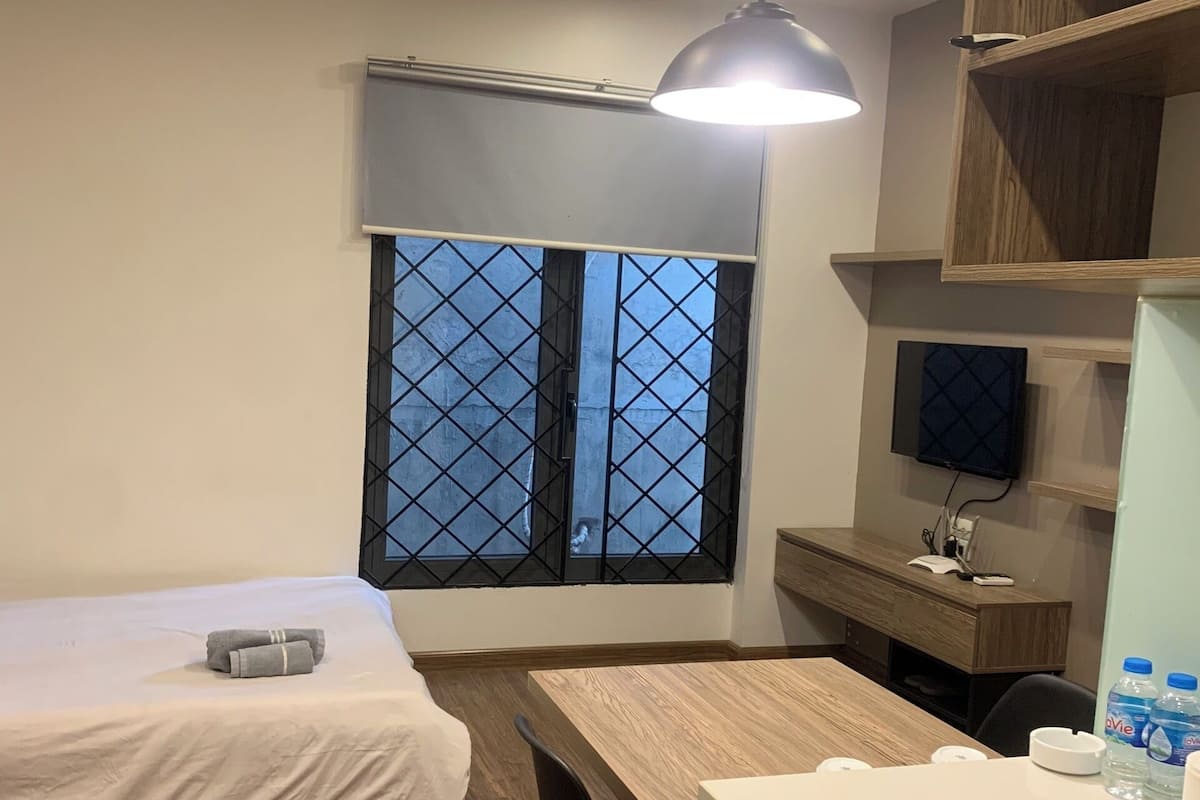 A hotel room with a bed, a desk, a chair, a TV, and a window with a view.